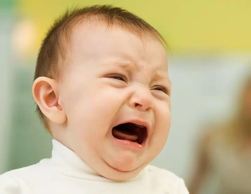 Visage d'un bébé en pleurs exprimant un inconfort ou une douleur, illustrant les signes comportementaux d'une piqûre d'insecte ou d'araignée chez le nourrisson